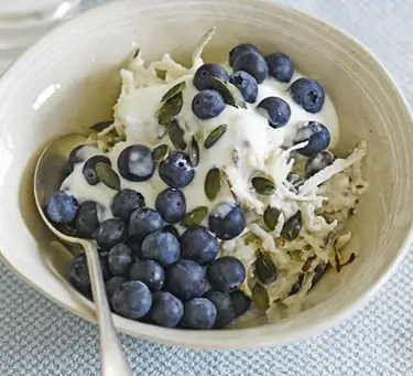 An image of porridge in a bowl with blueberries and pumpkin seeds on top.