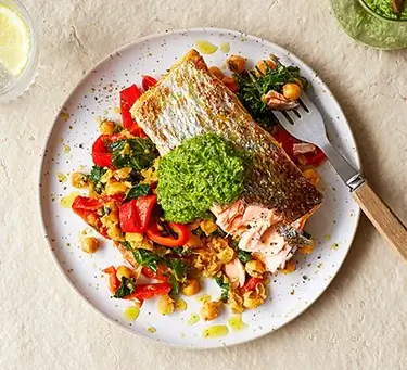 An image of salmon on top of a salad on a plate.